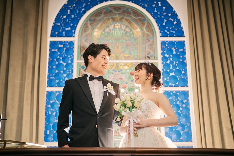グリーンの装飾で彩られた赤い大階段を降りるタキシードとウェディングドレスのふたり