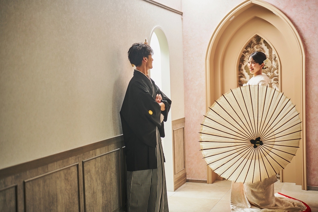 アーチの前で白い和傘を差す白無垢の花嫁と背中を向ける黒紋付袴の新郎。横浜店のスタジオで撮るファーストミートの和装前撮り