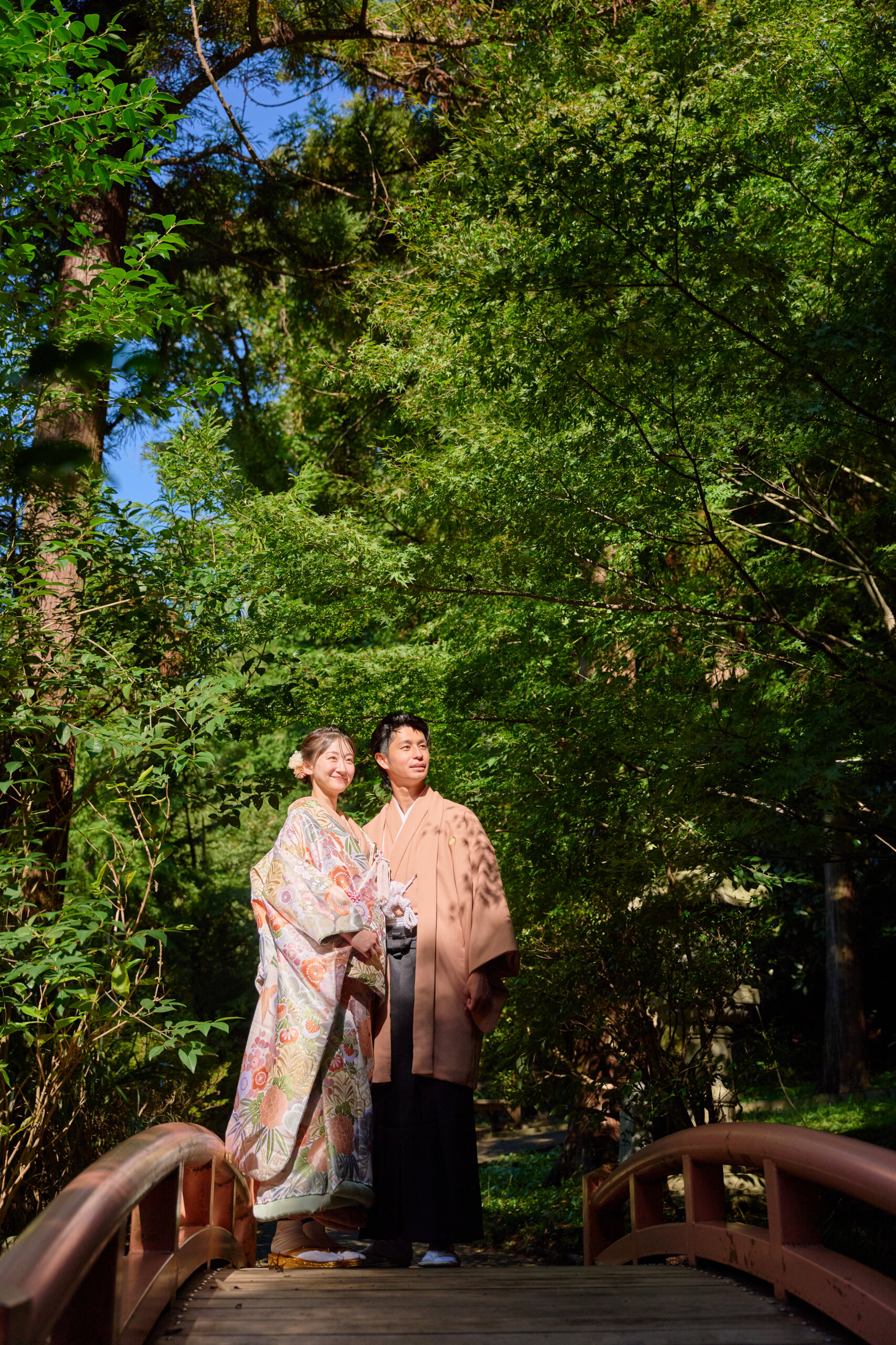 緑豊かな木々を背景に橋の上に立つ和装の新郎新婦