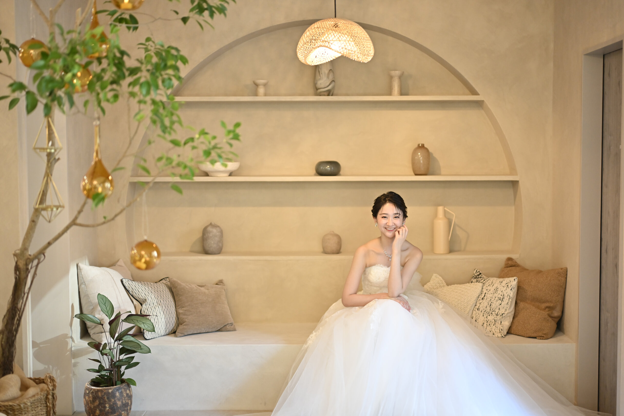 アーチ型の飾り棚のあるベージュの部屋のソファでドレスを広げて座るウェディングドレスの花嫁。横浜店のスタジオで撮る洋装前撮りのブライダルポートレート