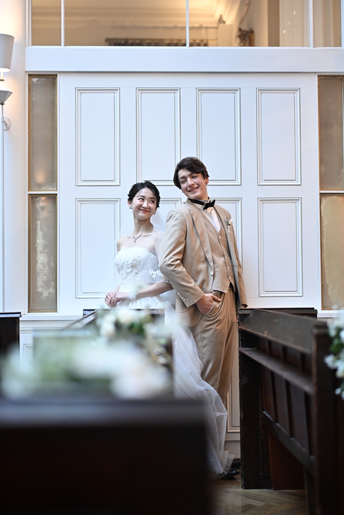 白いパネル壁を背景に寄り添いながら微笑み合う新郎新婦