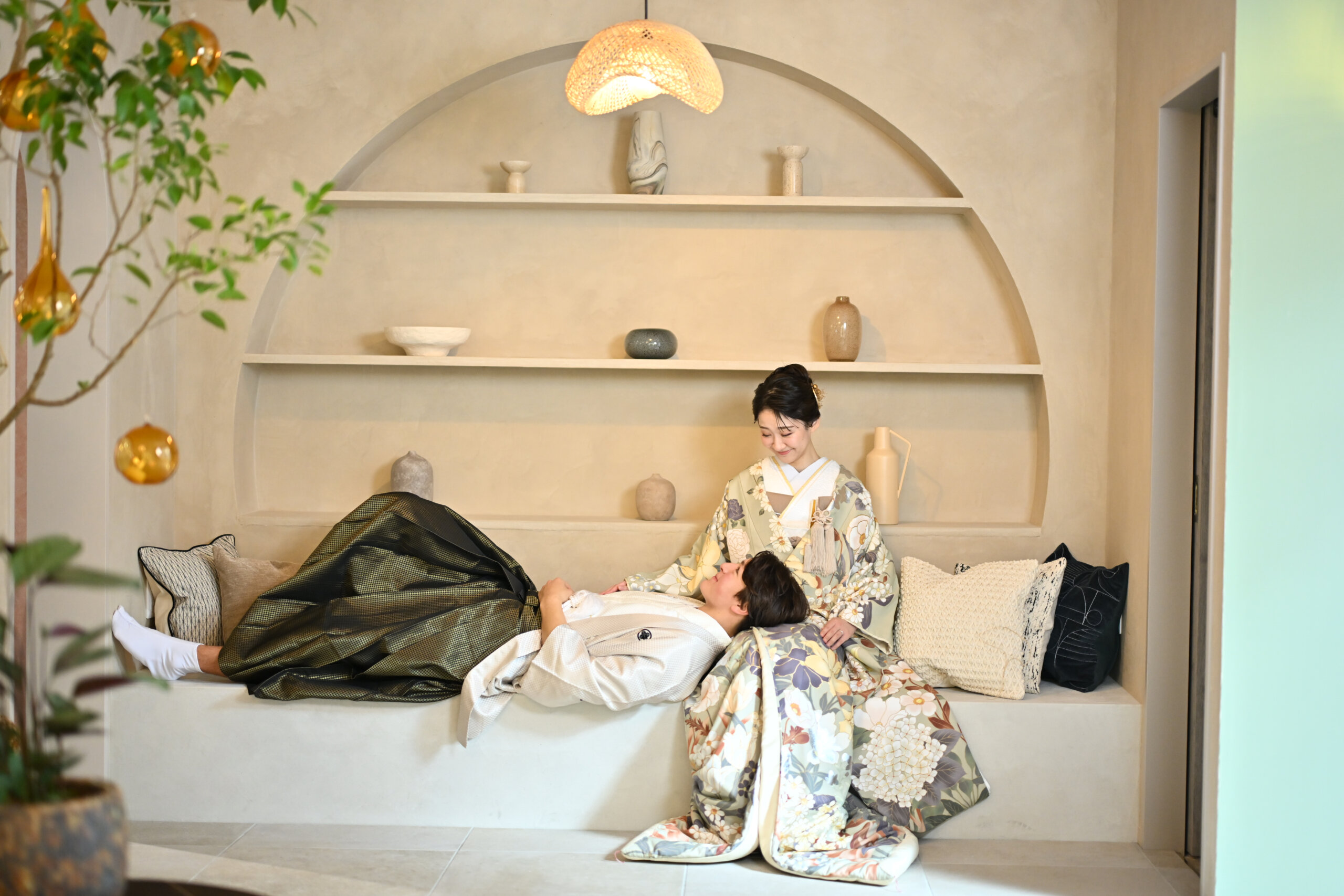 アーチ型の飾り棚のあるベージュの部屋のソファで新郎の膝枕をする花柄の色打掛の花嫁。横浜店のスタジオで撮る和装前撮りの遊び心のあるカット