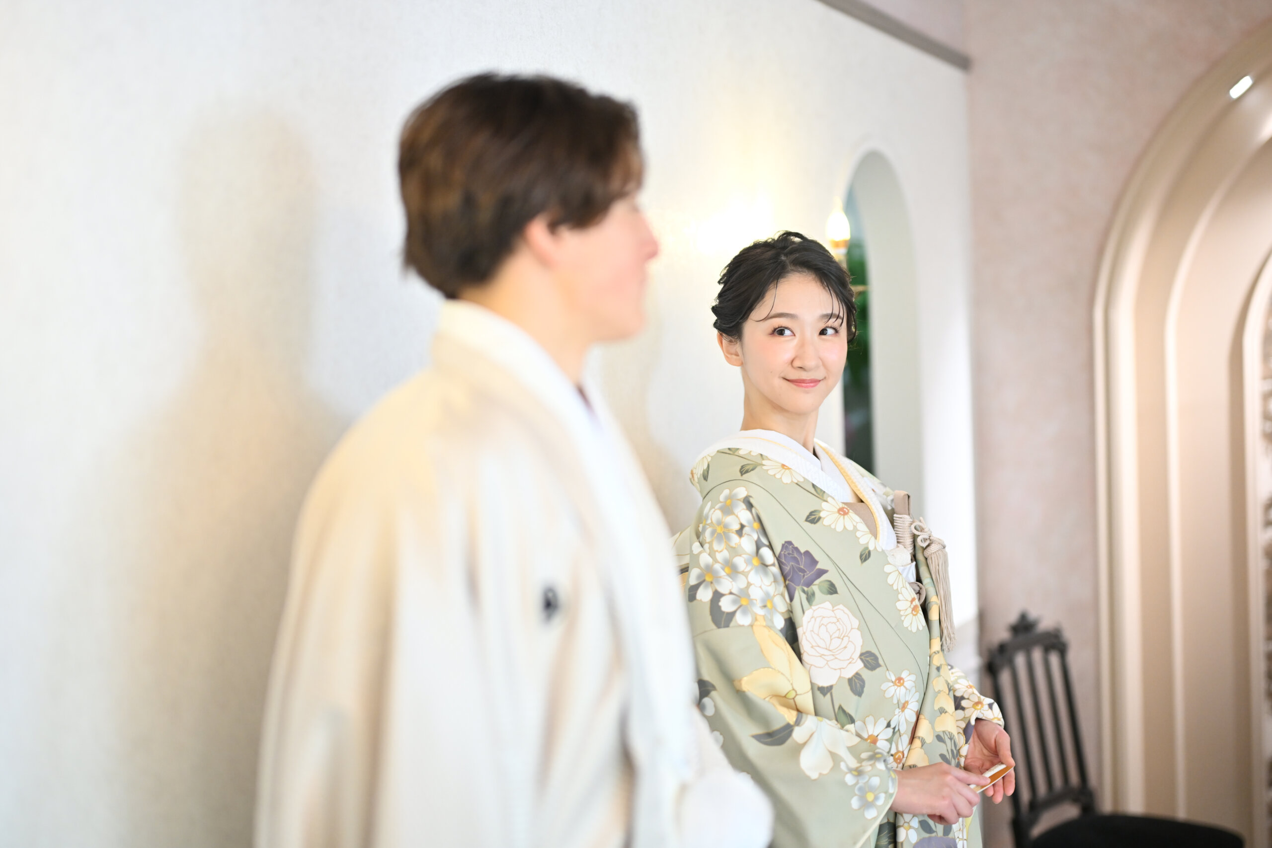 白い羽織の新郎の肩越しに微笑む淡いグリーンの花柄の色打掛の花嫁。横浜店のスタジオで撮る和装前撮り