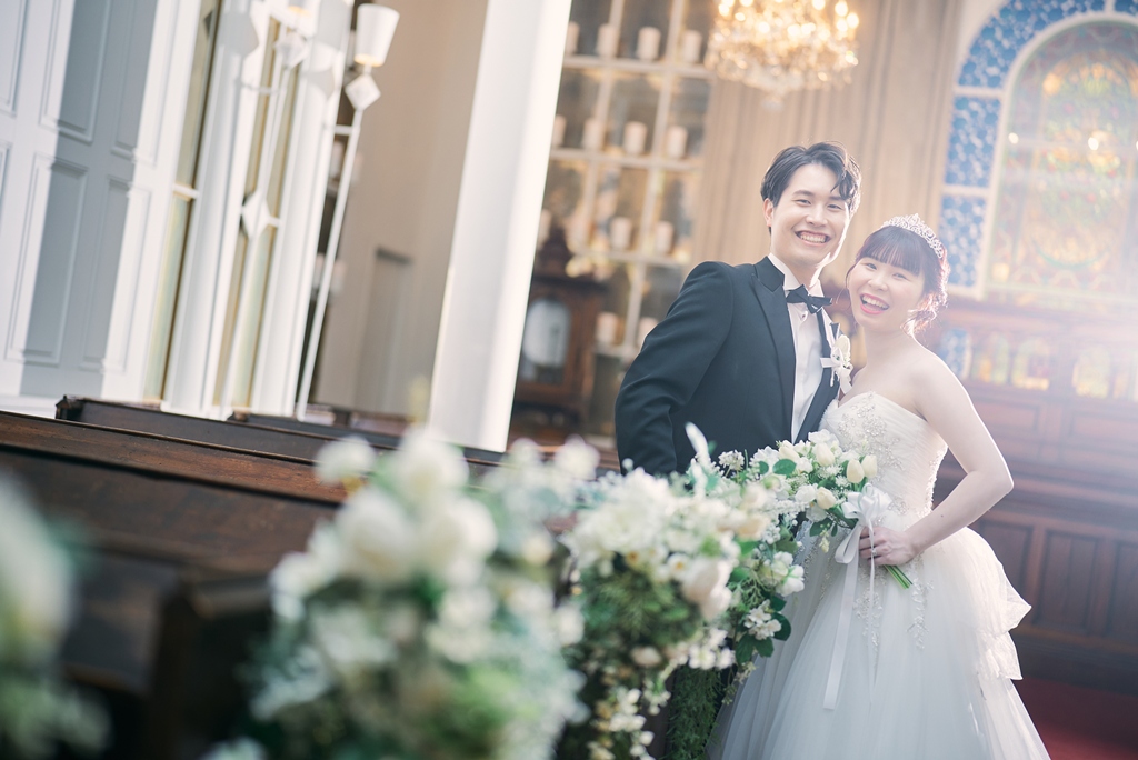 青いステンドグラスを背景に祭壇の前で微笑み合う新郎新婦