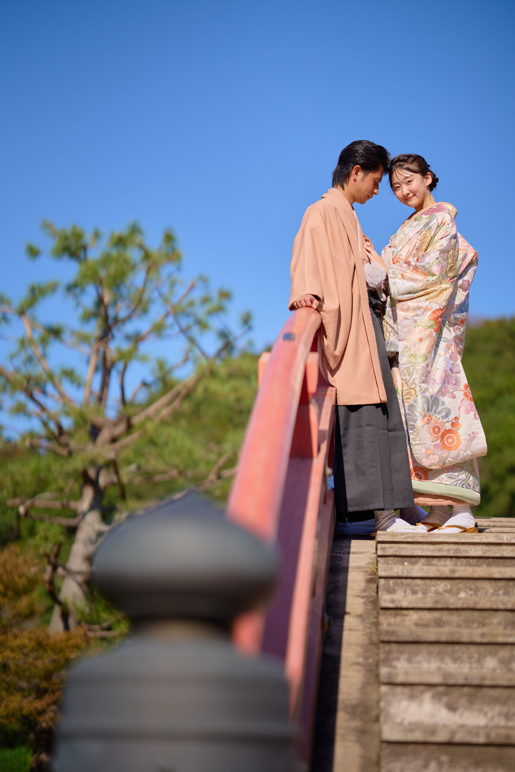 橋の欄干にもたれながら額を寄せ合う和装の新郎新婦