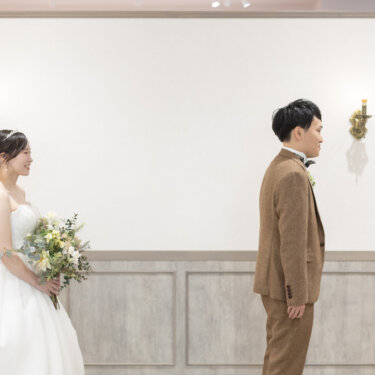 背中を向けて待つ新郎と、その後ろでほほえむウェディングドレスの花嫁。ファーストミート直前の横浜のスタジオ前撮り