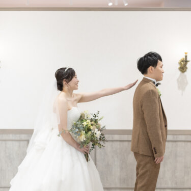 後ろ向きに立つ新郎の肩に手を伸ばす、ブーケを持った花嫁。ドキドキのファーストミート演出の前撮り