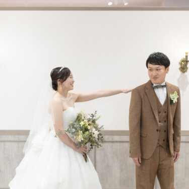 背を向けた新郎の肩をトントンとたたく花嫁。ファーストミートの始まりを写した横浜のスタジオフォト