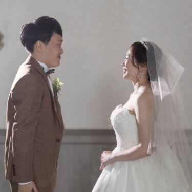 燭台のある白い壁の前で向かい合い、笑顔を交わす新郎新婦。ベールをまとったウェディングドレスで撮る横浜のスタジオ前撮り