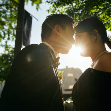 並木の木漏れ日の中、逆光でキスする寸前の新郎新婦の横顔。光が差し込むロマンチックなウェディングフォト