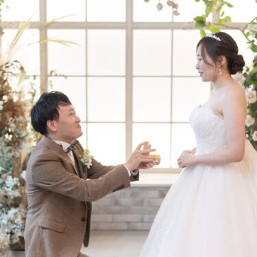 窓辺の花のセットでひざまずき、リングケースを差し出す新郎を見つめる花嫁。横浜のスタジオで撮るプロポーズの前撮り