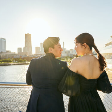 みなとみらいの高層ビルと夕日を眺めながら寄り添う新郎新婦の後ろ姿。手すり越しに海を望む大さん橋のウェディングフォト