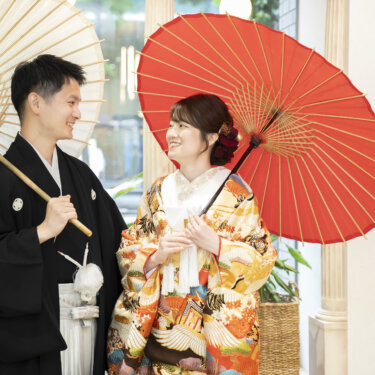 白と赤の和傘を差して見つめ合う黒紋付袴の新郎と色打掛の花嫁。和傘を使った横浜のスタジオ和装前撮り