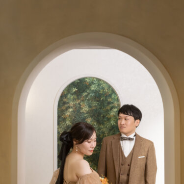 アーチ型の入口越しに寄り添う新郎と、リボンのヘアアレンジのカラードレスの花嫁。奥行きのある構図で撮る横浜のスタジオ前撮り