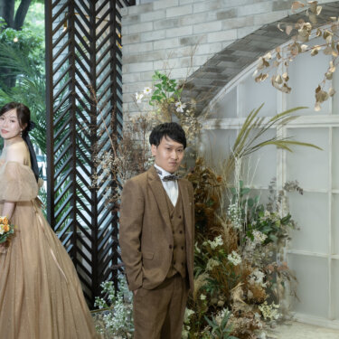 緑と草花に囲まれたアーチ窓のセットに並ぶ、ベージュのボリュームドレスの花嫁と新郎。横浜のスタジオで撮るナチュラルなフォトウェディング