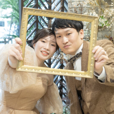 金色の額縁を二人で持ち、フレームの中から顔を寄せる新郎新婦。小物を使った横浜のスタジオ前撮りで人気のポーズ