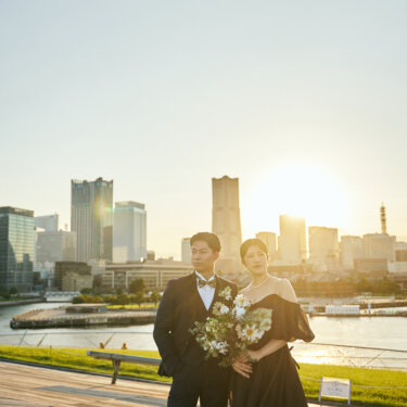 ランドマークタワーと夕日を背に寄り添う新郎新婦。大さん橋のウッドデッキで撮る逆光のロケーションフォト