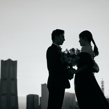 ランドマークタワーのシルエットを背景に、ブーケを手に向かい合う新郎新婦。モノクロで仕上げた大人っぽい結婚写真
