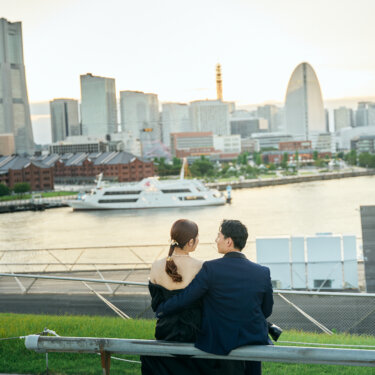 赤レンガ倉庫とみなとみらいの街並みを眺めながらベンチに並んで座る新郎新婦の後ろ姿。横浜らしい景色のロケーションフォト