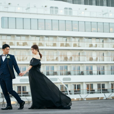 大型客船を背景に手をつないで歩き出す新郎新婦。風に揺れる黒いカラードレスが映える大さん橋のウェディングフォト