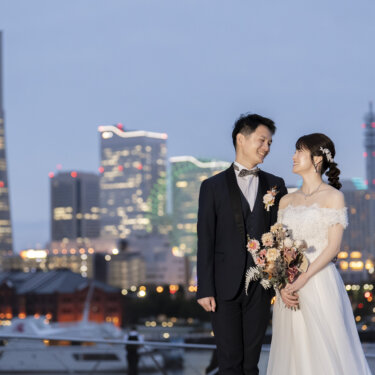 夕暮れのみなとみらいの夜景と赤レンガ倉庫を背に微笑み合う新郎新婦。大さん橋から撮る横浜の洋装フォトウェディング