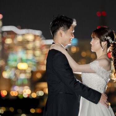 色とりどりの夜景のボケの中で見つめ合い抱き合うネイビースーツの新郎と花嫁。夜景を使ったロマンチックなフォトウェディング
