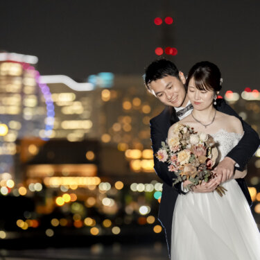 夜景のボケを背に、ドライフラワーのブーケを持つ花嫁を後ろから抱きしめる新郎のバックハグ。夜の前撮りで人気のポーズ