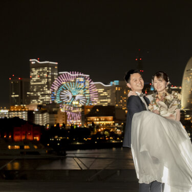 ランドマークタワーと観覧車の夜景を背に、花嫁をお姫様抱っこする新郎。横浜の夜の前撮りで人気のポーズ