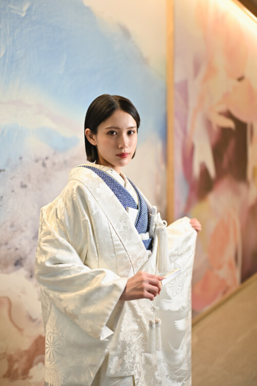淡い色彩のアートウォールの前で白無垢の袖を手にする花嫁。和装フォトウェディングの一枚