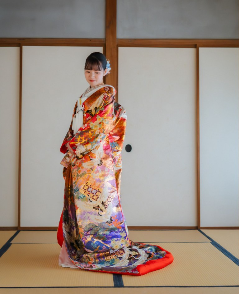 金と紫に彩られた吉祥文様の色打掛をまとい、障子の和室で畳に引き裾を流して佇む花嫁。横浜店の和装前撮り（紫鶴／衣装番号YB15）