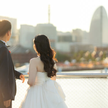 赤レンガ倉庫とみなとみらいのビル群を眺める新郎新婦の後ろ姿を、やわらかな逆光で撮ったロケーションフォト
