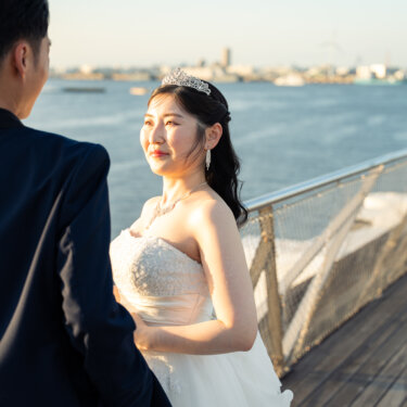 海を見渡すデッキの手すり沿いで、ティアラの花嫁が新郎越しに微笑む横浜の港の洋装前撮り