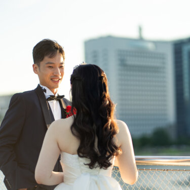大さん橋の手すりの前で笑顔の新郎と向かい合う、ダウンスタイルのヘアアレンジの花嫁の後ろ姿が印象的な結婚写真