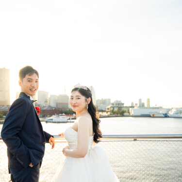 横浜港の客船とランドマークタワーを背景に、振り返って笑う新郎新婦のナチュラルな前撮り