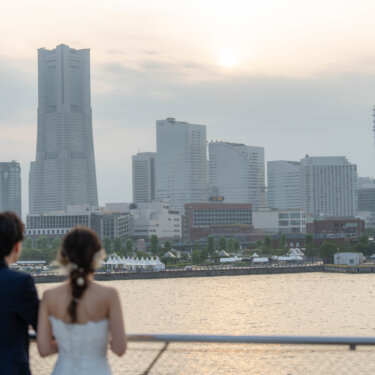 夕暮れのみなとみらいのビル群と海を眺める新郎新婦の後ろ姿。大さん橋から撮るロケーションフォトで人気の構図