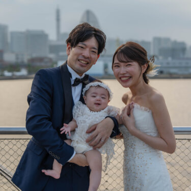 大さん橋のデッキで白いドレスの赤ちゃんを抱いて笑う新郎新婦。横浜の景色と撮る親子フォトのフォトウェディング