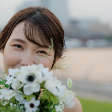 白いアネモネのブーケを顔の横に寄せてほほえむ花嫁のアップ。海辺の夕暮れに撮る洋装前撮りのブーケショット