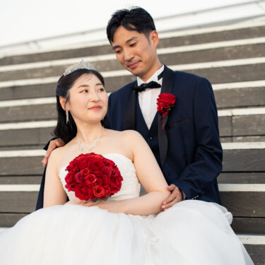階段に座る花嫁を後ろから新郎が包み込み、赤いバラのブーケを抱いて微笑む横浜の前撮り
