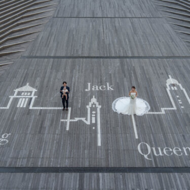KINGとQUEENとJACKの文字が描かれたウッドデッキに立つ新郎新婦を俯瞰で写した一枚。大さん橋ならではの遊び心ある前撮りの構図