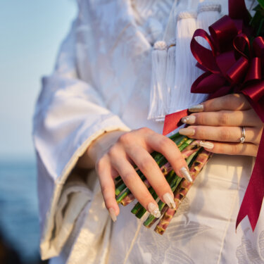 白無垢の花嫁が手にする赤いリボンのブーケと筥迫、指先の結婚指輪のアップ。海辺で撮る和装前撮りの小物カット