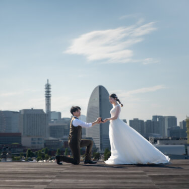 観覧車とランドマークタワーが並ぶみなとみらいを背に、片膝をついて花嫁の手を取る新郎。大さん橋で撮るプロポーズ再現の前撮り