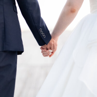 タキシードの新郎とウェディングドレスの花嫁が手をつなぐ手元だけを切り取った、シンプルで上品な結婚写真