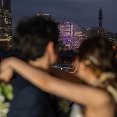 首に腕をまわして抱き合う新郎新婦の肩越しに広がる、みなとみらいの観覧車の夜景。ロマンチックなナイトフォトの前撮り
