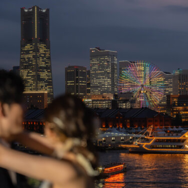 観覧車とランドマークタワーの夜景を前ぼけの新郎新婦越しに写した一枚。横浜みなとみらいの夜景が主役のフォトウェディング