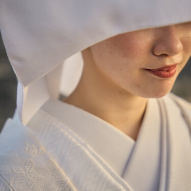 綿帽子の下からのぞく白無垢の花嫁の口元と襟元のアップ。白無垢の織り柄が映える和装前撮りのディテールカット