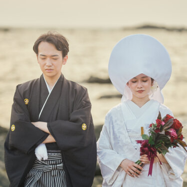 夕暮れの海を背に、腕を組む紋付袴の新郎と綿帽子に赤いブーケを持つ白無垢の花嫁。城ヶ島で撮る和装前撮り