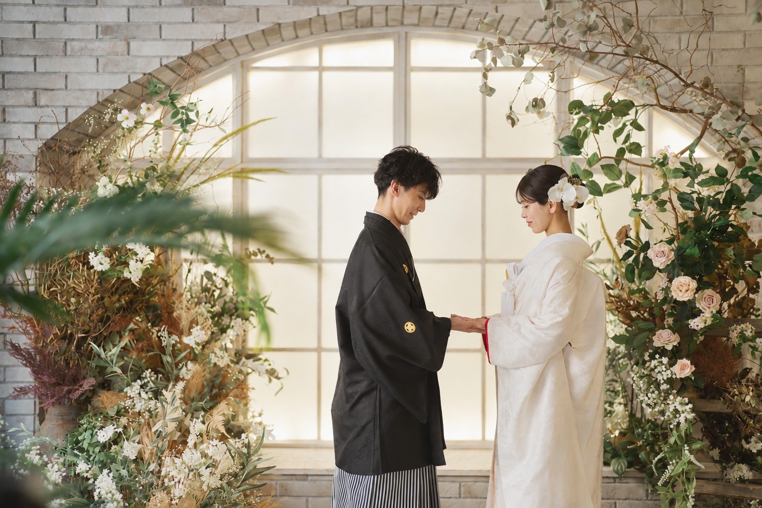 光の差すレンガのアーチ窓の前で手を取り合う黒紋付袴の新郎と白無垢の花嫁。横浜リゾートスタジオの和装スタジオフォト
